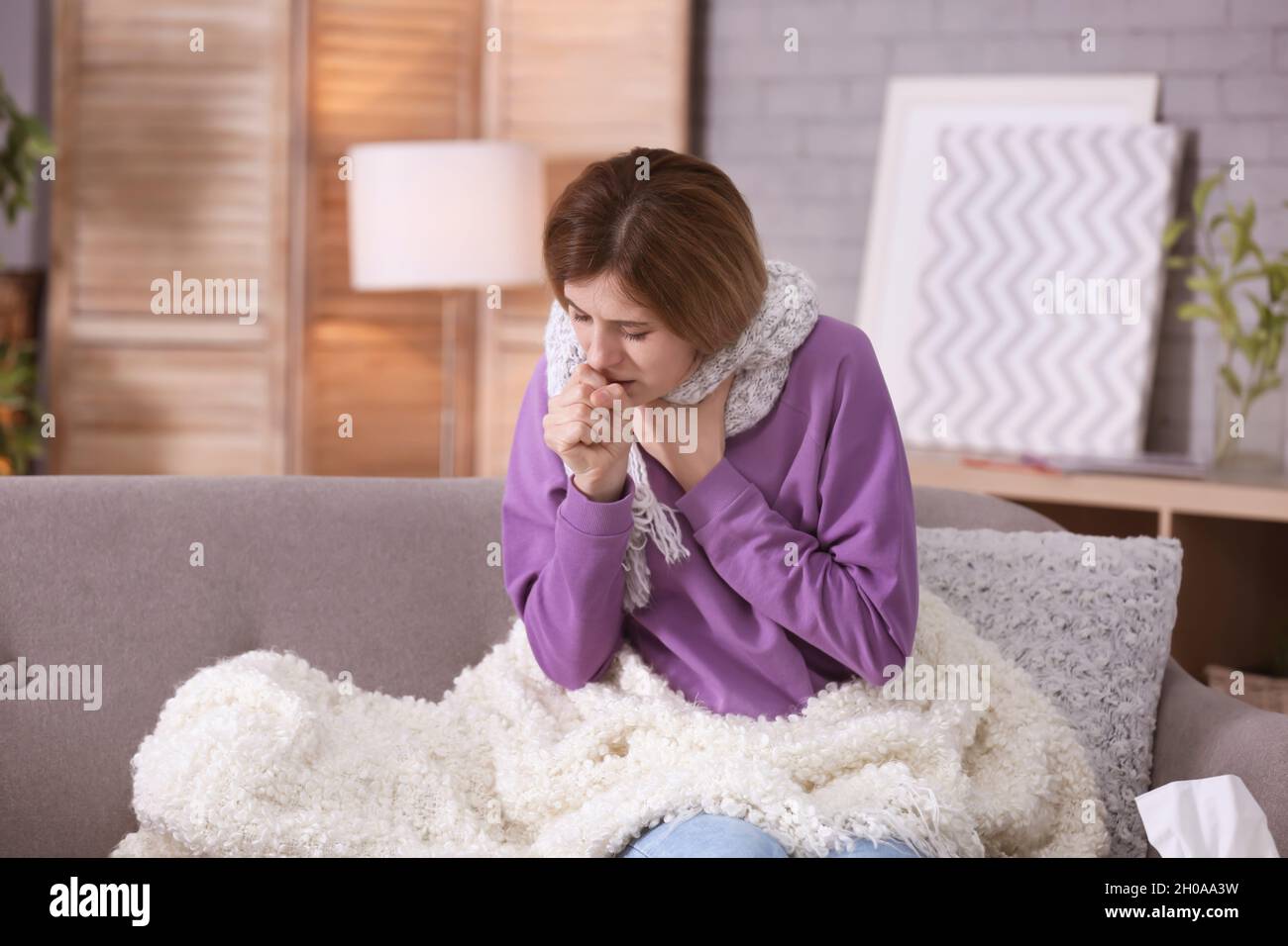 Sick woman with cough suffering from cold on sofa at home Stock Photo