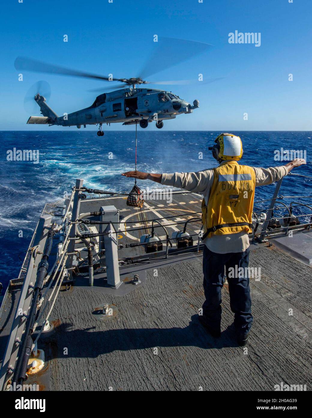 PACIFIC OCEAN (Jan. 9, 2021) U.S. Navy Boatswain’s Mate Seaman Javough Watson, from Plainfield, N.J., signals the pilot of an MH-60R Sea Hawk, assigned to the “Magicians” of Helicopter Maritime Strike Squadron (HSM) 35, to lower supplies to the flight deck of the Arleigh Burke-class guided-missile destroyer USS John Finn (DDG 113) Jan. 9, 2021. John Finn, part of the Theodore Roosevelt Carrier Strike Group, is on a scheduled deployment to the U.S. 7th Fleet area of operations. As the U.S. Navy’s largest forward deployed fleet, with its approximate 50-70 ships and submarines, 140 aircraft, and Stock Photo