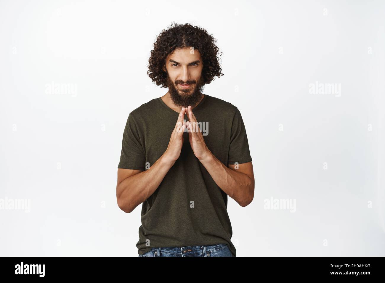 Greedy and devious middle eastern man scheming plan, steeple fingers like evil genius, idea in mind, standing over white background Stock Photo