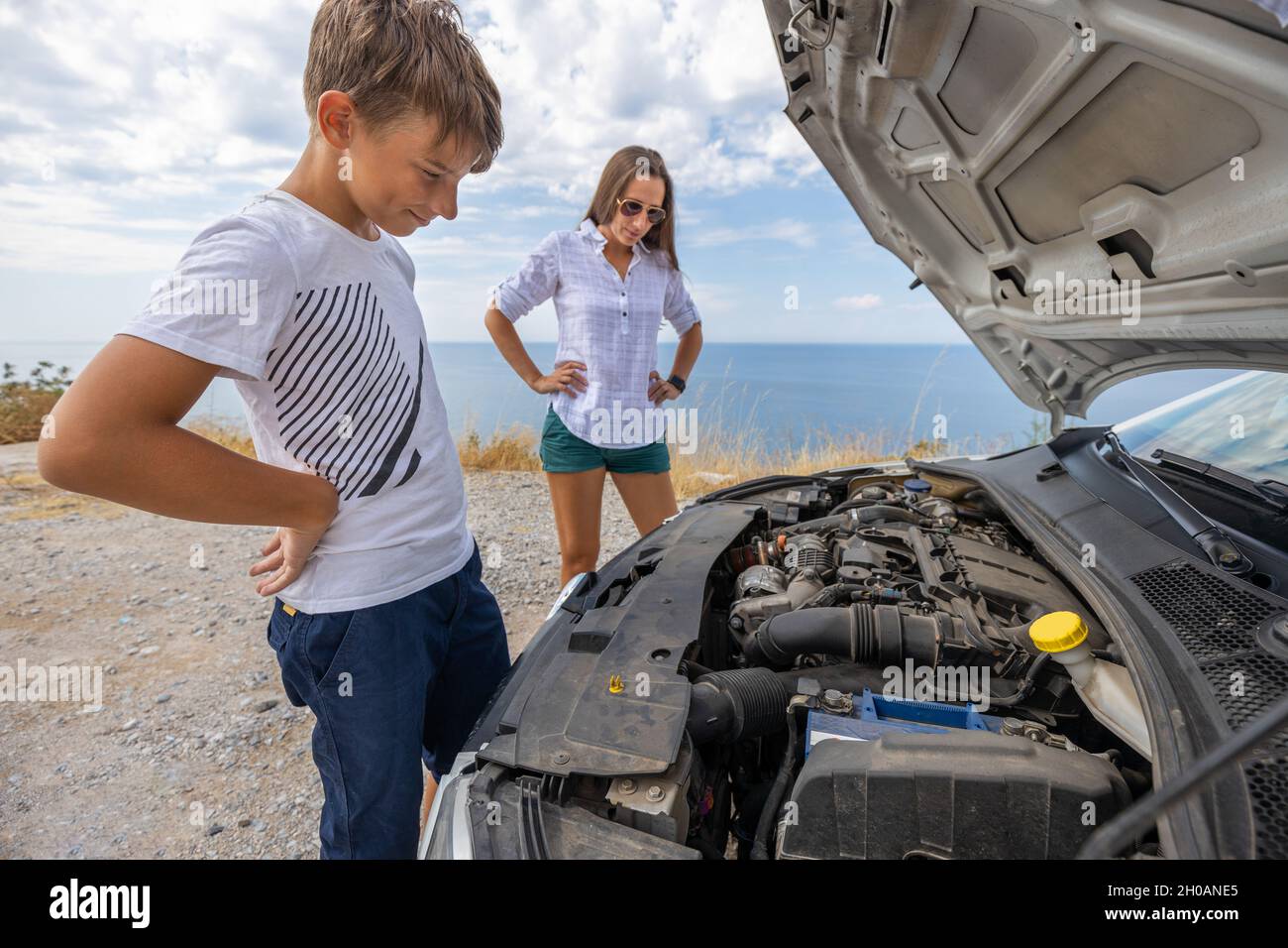 Teenage boy with his mother trying to fix broken rent car during summer vacation. Rent car insurance concept image Stock Photo