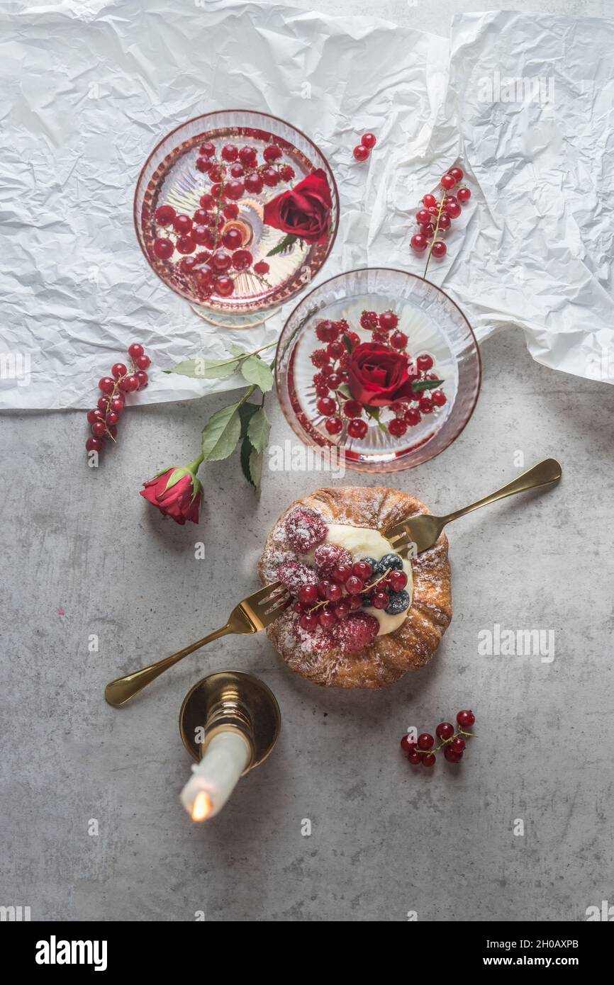 Two cocktails with red berries and rose blossom, pastry with berries