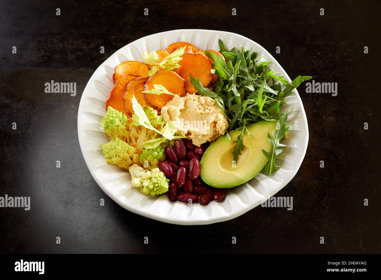 From above of vegetarian Buddha bowl with fresh assorted vegetables and hummus served on black table for healthy lunch Stock Photo