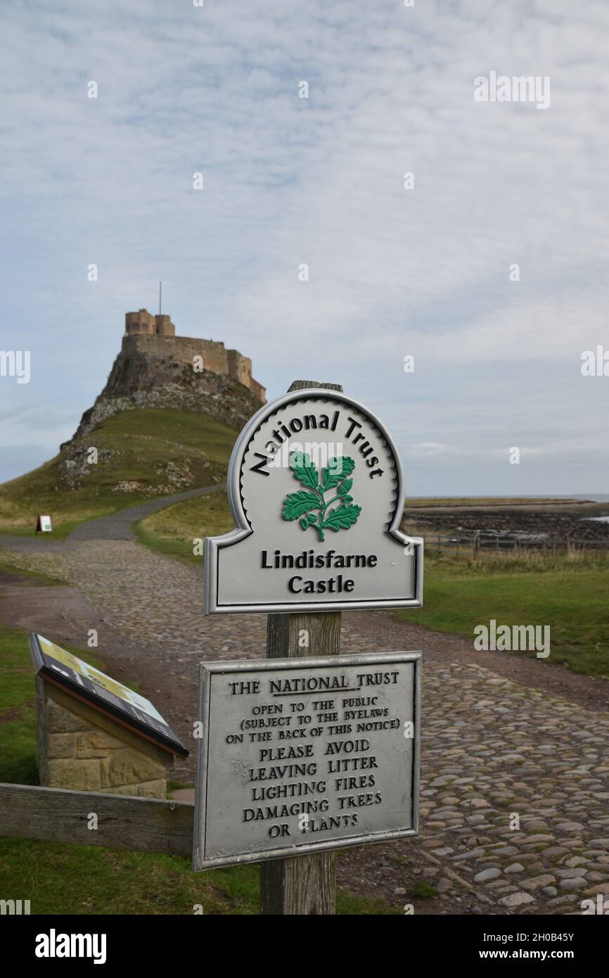 Sign for Lindisfarne Castle with blurred background of path, castle and blue sky with clouds. Shallow depth of field. Stock Photo