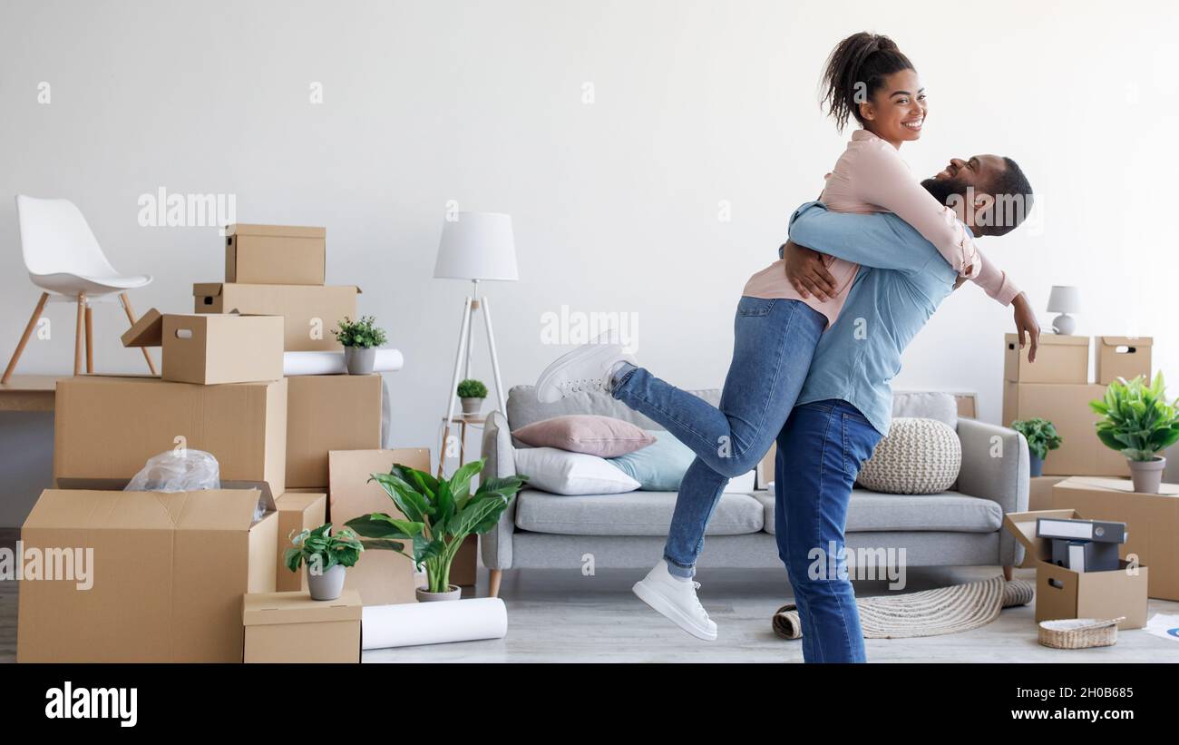Glad millennial african american husband hugs and lifts his wife in new ...