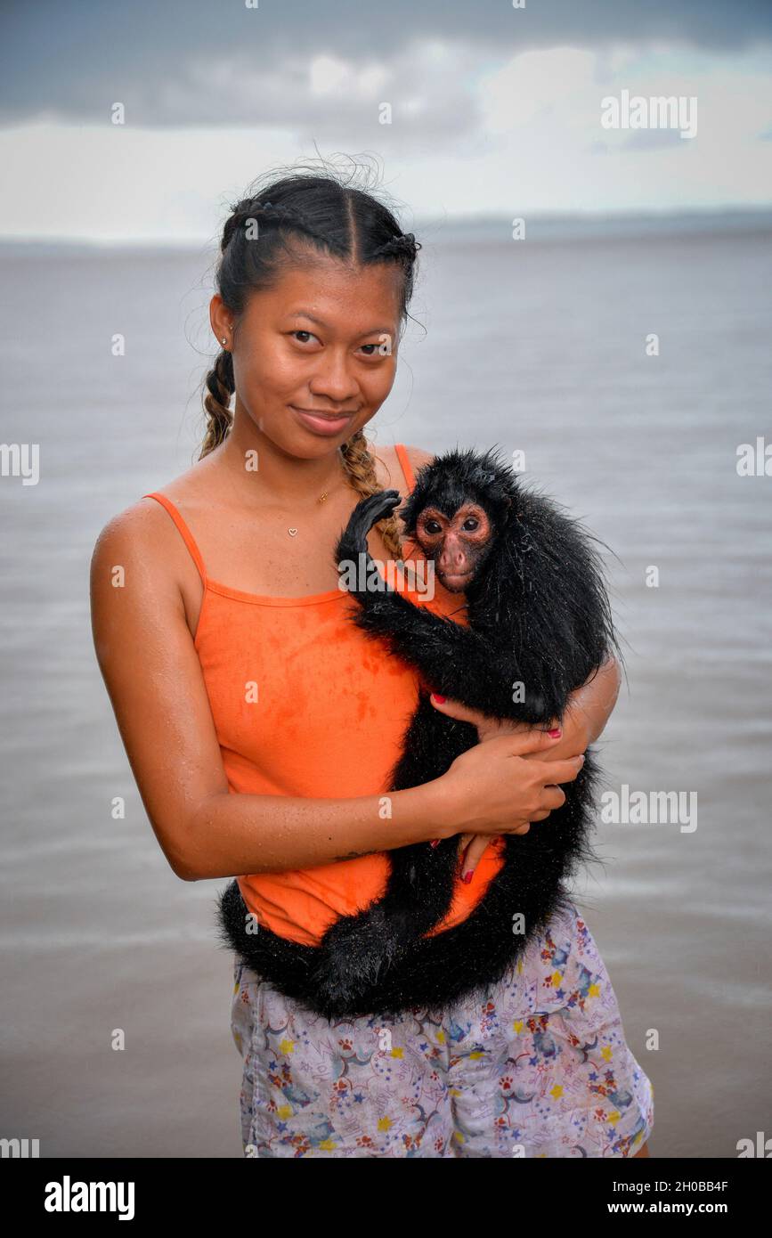 Young black spider monkey (Ateles paniscus) in the arms of a young woman in the rain in French Guiana Stock Photo