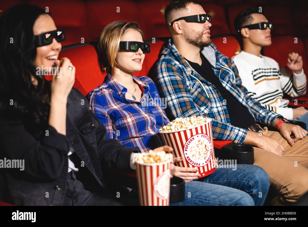 Friends are watching a movie in the cinema. People sit in the armchairs of the cinema and look at the screen with special glasses for 3D Stock Photo
