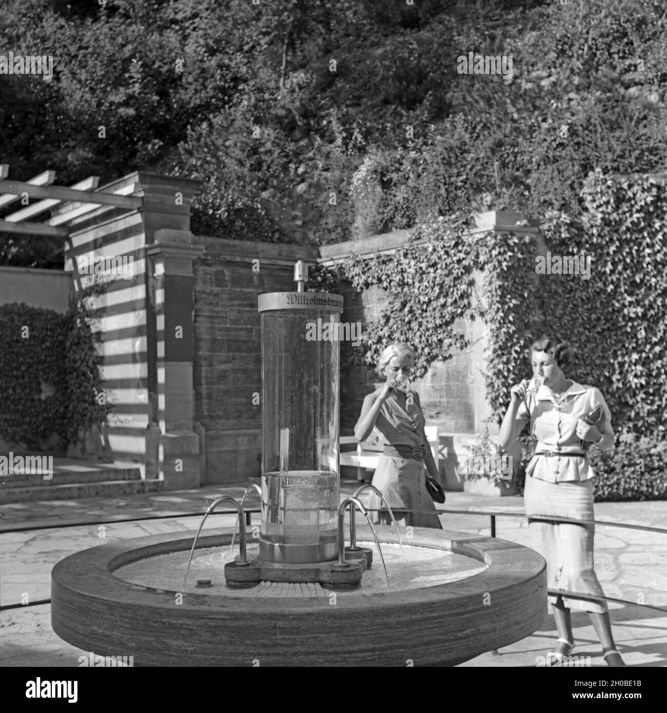 Zwei Frauen trinken aus dem Wilhelmsbrunnen in Bad Cannstatt, Deutschland 1930er Jahre. Two women drinking water from the Wilhelmsbrunnen well at Bad Cannstatt, Germany 1930s. Stock Photo