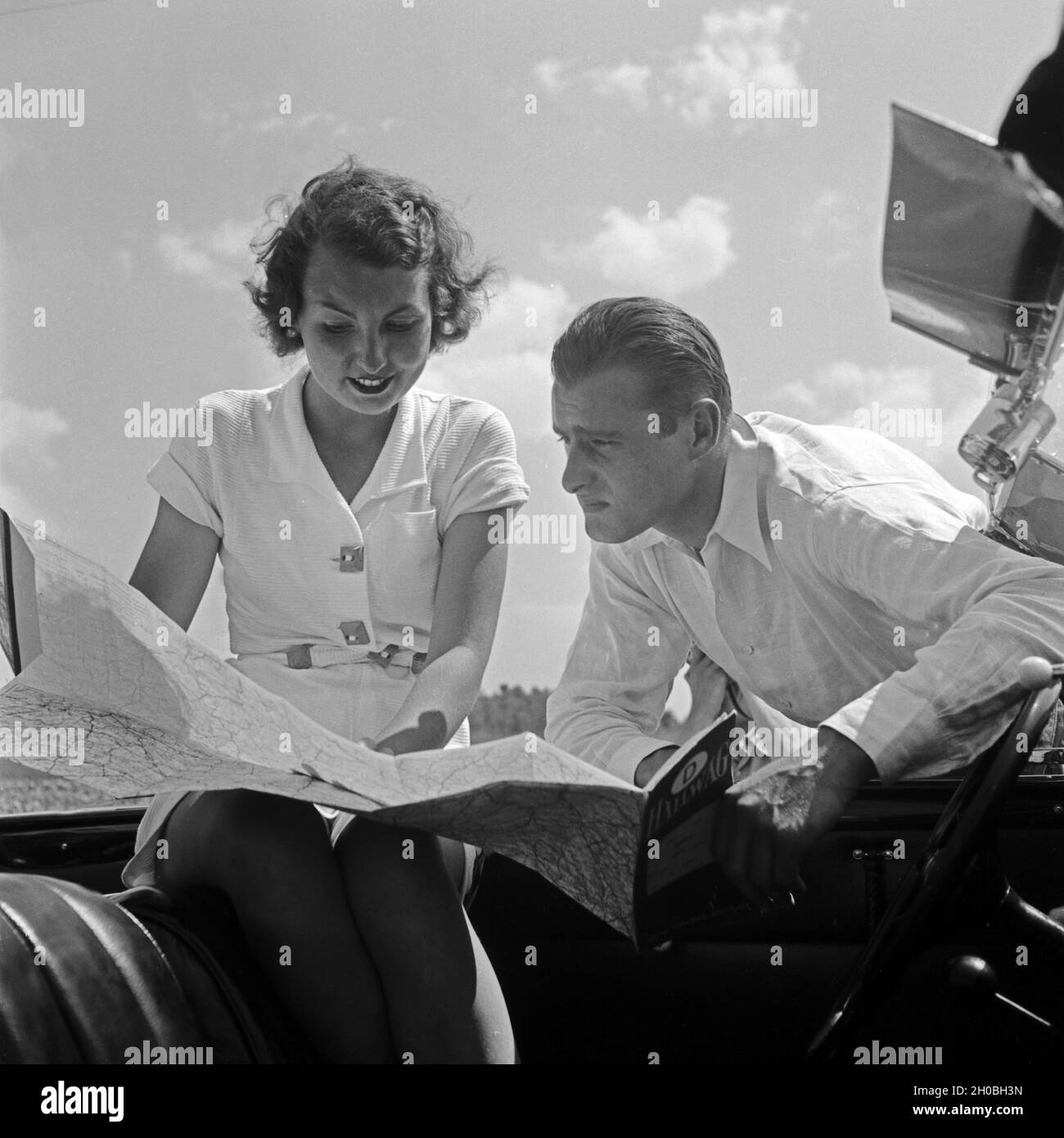 Ein junger Mann und eine junge Frau ziehen bei einer Autofahrt die Hallwag Straßenkarte zu Rate, Deutschland 1930er Jahre. A young couple using the Hallwag road map, Germany 1930s. Stock Photo