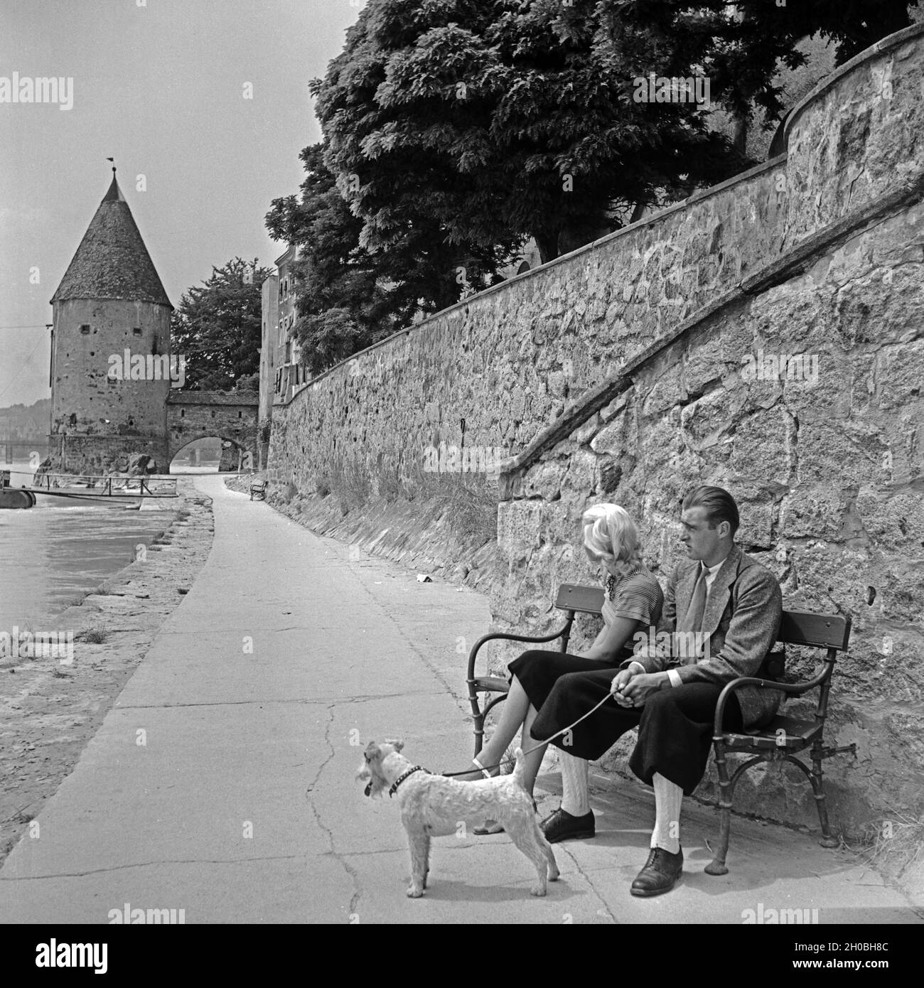 Ein junges Paar sitzt auf einer Bank am Innkai nahe am Schaiblingturm in Passau, Deutschland 1930er Jahre. A young couple sitting on a bench at Innkai quay near Schaiblingsturm tower at Passau, Germany 1930s. Stock Photo