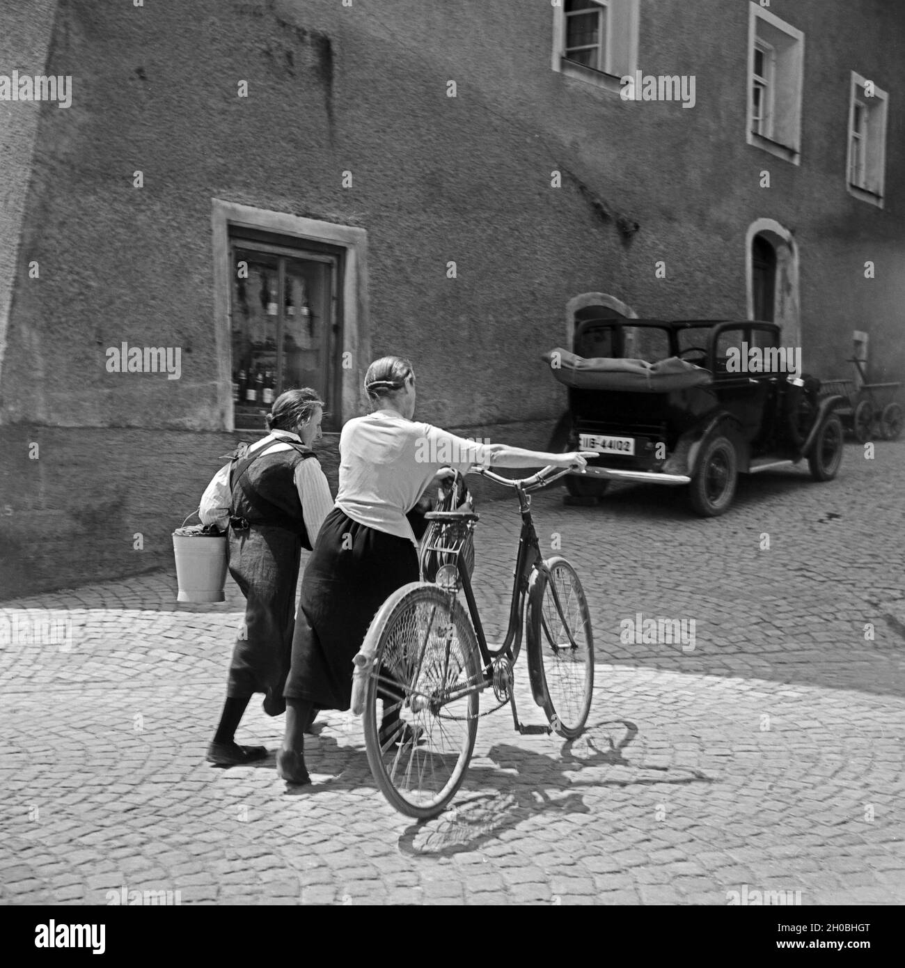 Zwei Frauen schieben ein Fahrrad durch die Gassen von Burghausen, Deutschland 1930er Jahre. Two women on their way home through the lanes of Burghausen, Germany 1930s. Stock Photo
