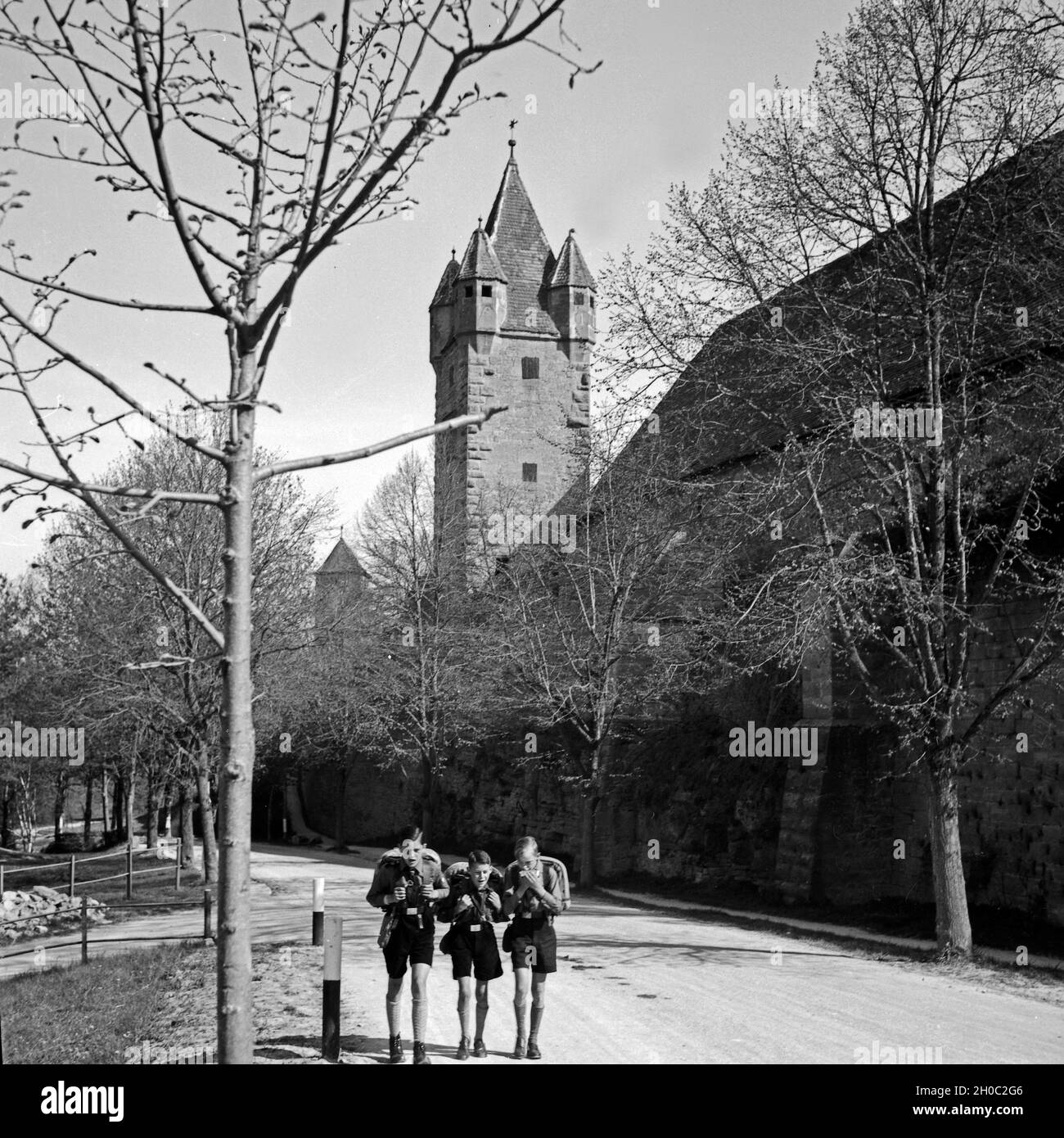 Drei Hitlerjungen auf einer Wandertour durch Deutschland an einer Stadtmauer mit Stadtturm, 1930er Jahre. Three Hitler youths wandering through Germany near a city wall and watchout. 1930s. Stock Photo