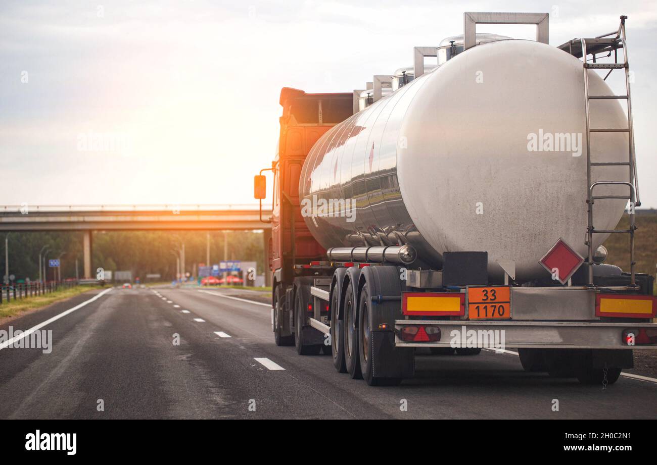 A truck with a tank trailer transports a liquid dangerous cargo on a highway against the backdrop of a sunset. Stock Photo
