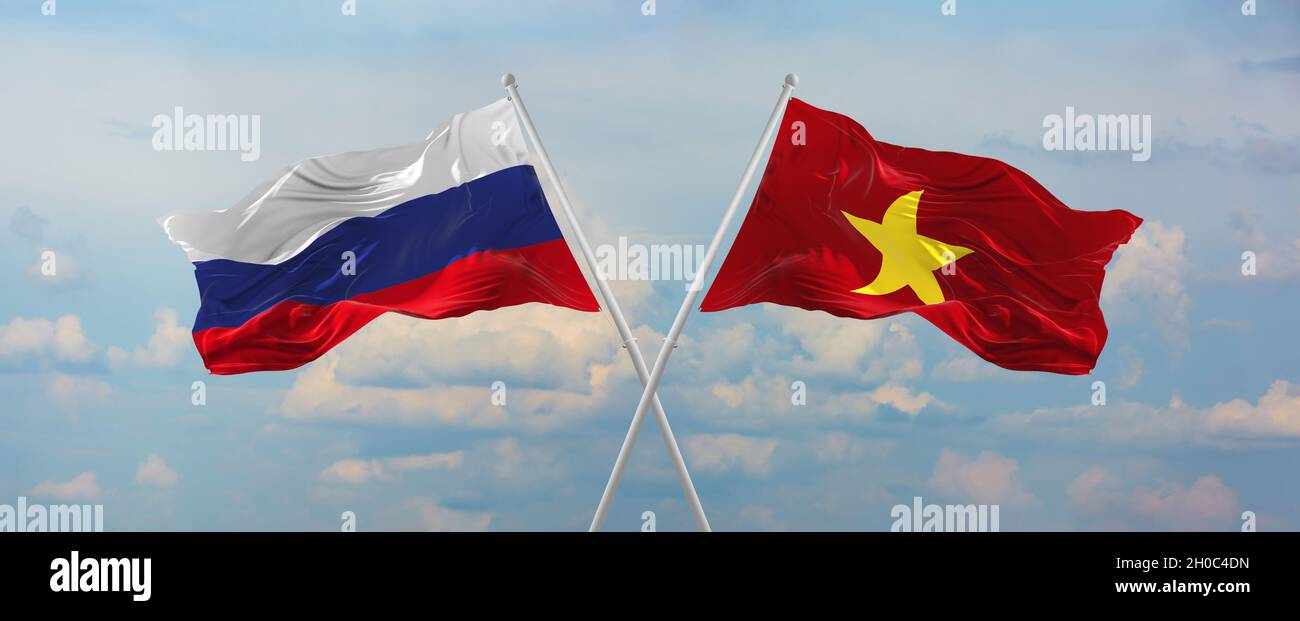 flags of Russia and Vietnam waving in the wind on flagpoles against sky with clouds on sunny day. Symbolizing relationship, dialog between two countri Stock Photo