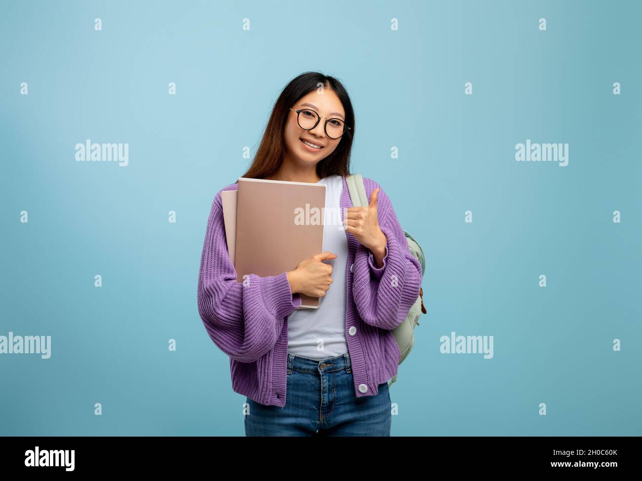 Positive asian female student holding workbooks and showing thumb up ...