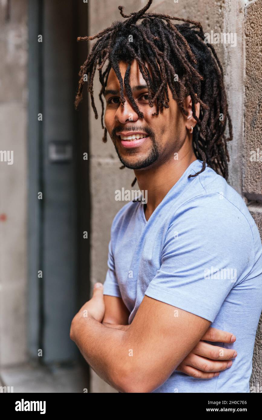 vertical portrait of an hispanic young man with dreadlocks. He is looking at camera and smiles Stock Photo