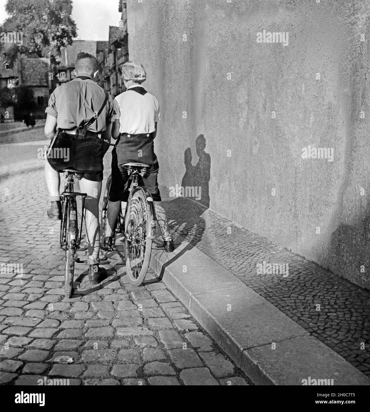 Ein Hitlerjunge und ein BDM Mädel auf ihren Fahrrädern in einer Gasse in Braunschweig, Deutschland 1930er Jahre. A Hitler youth and a BDM girl on their bicycles in a lane of Braunschweig, Germany 1930s. Stock Photo