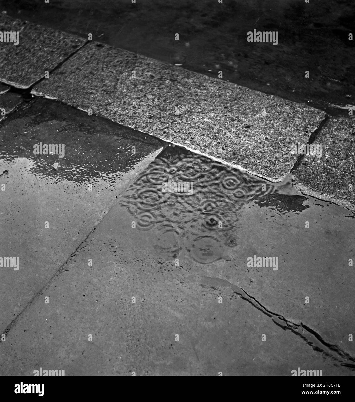 Regentropfen fallen in eine Pfütze auf einem Bürgersteig in Braunschweig, Deutschland 1930er Jahre. Raindrops falling into a puddle at the pavement of Braunschweig, Germany 1930s. Stock Photo
