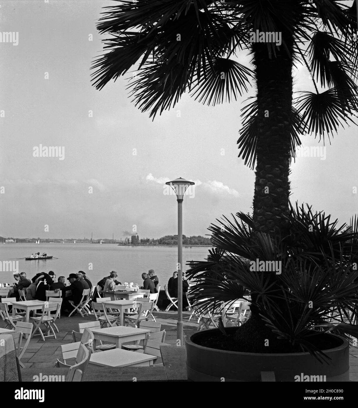 Menschen erfrischen sich in der von Palmen umgebenen Außengastronomie am Maschsee bei Hannover, Deutschland 1930er Jahre. People relaxing at a garden restaurant on the shore of Maschsee lake near Hanover, Germany 1930s. Stock Photo