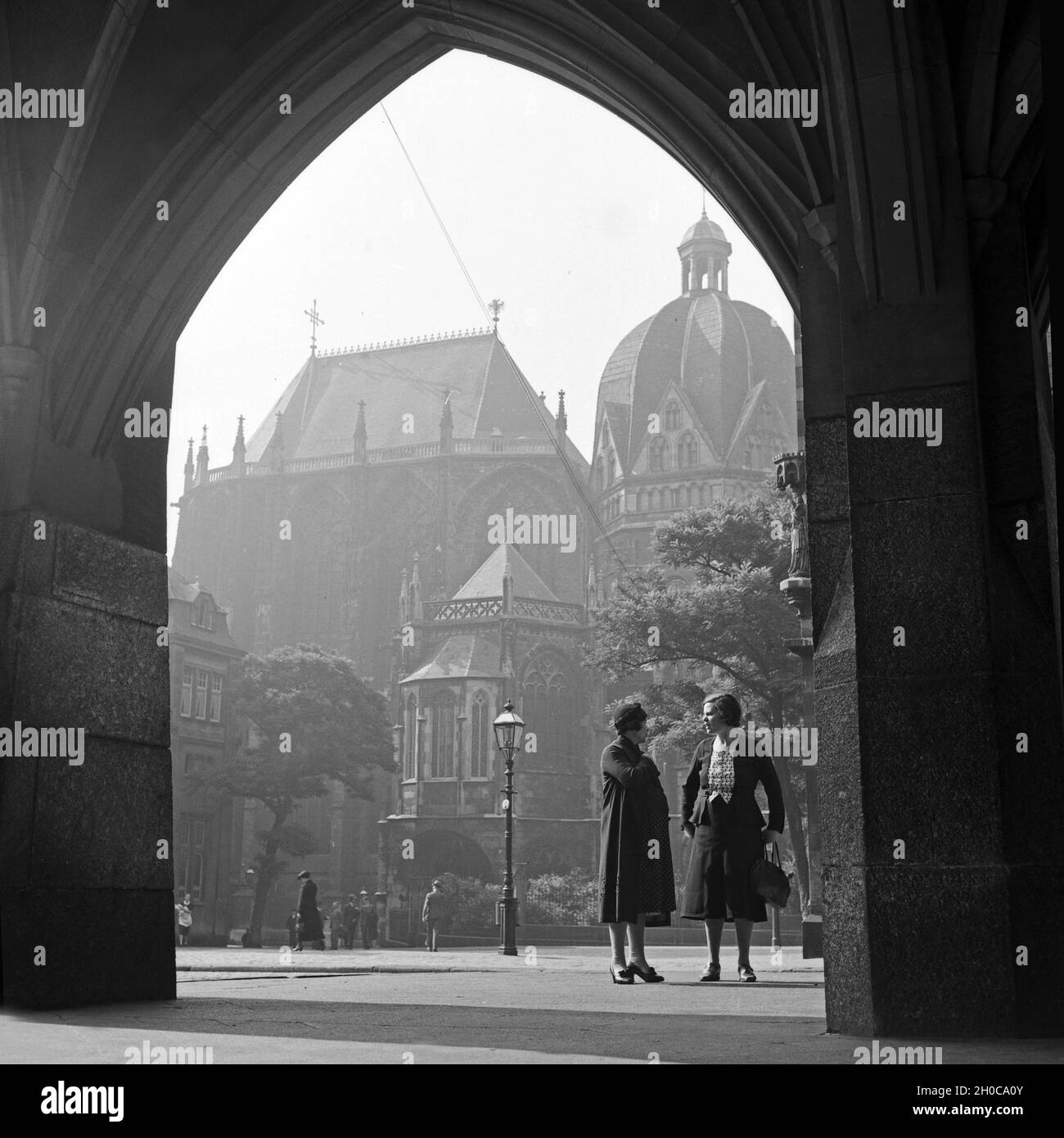 Zwei Frauen unterhalten sich im Kolonnadengang des Rathauses am Katschhof in Aachen mit dem Kaiserdom in Hintergrund, Deutschland 1930er Jahre. Two women chatting in the colonnades archway of the baroque style city hall at Aachen with the cathedral in the background, Germany 1930s. Stock Photo