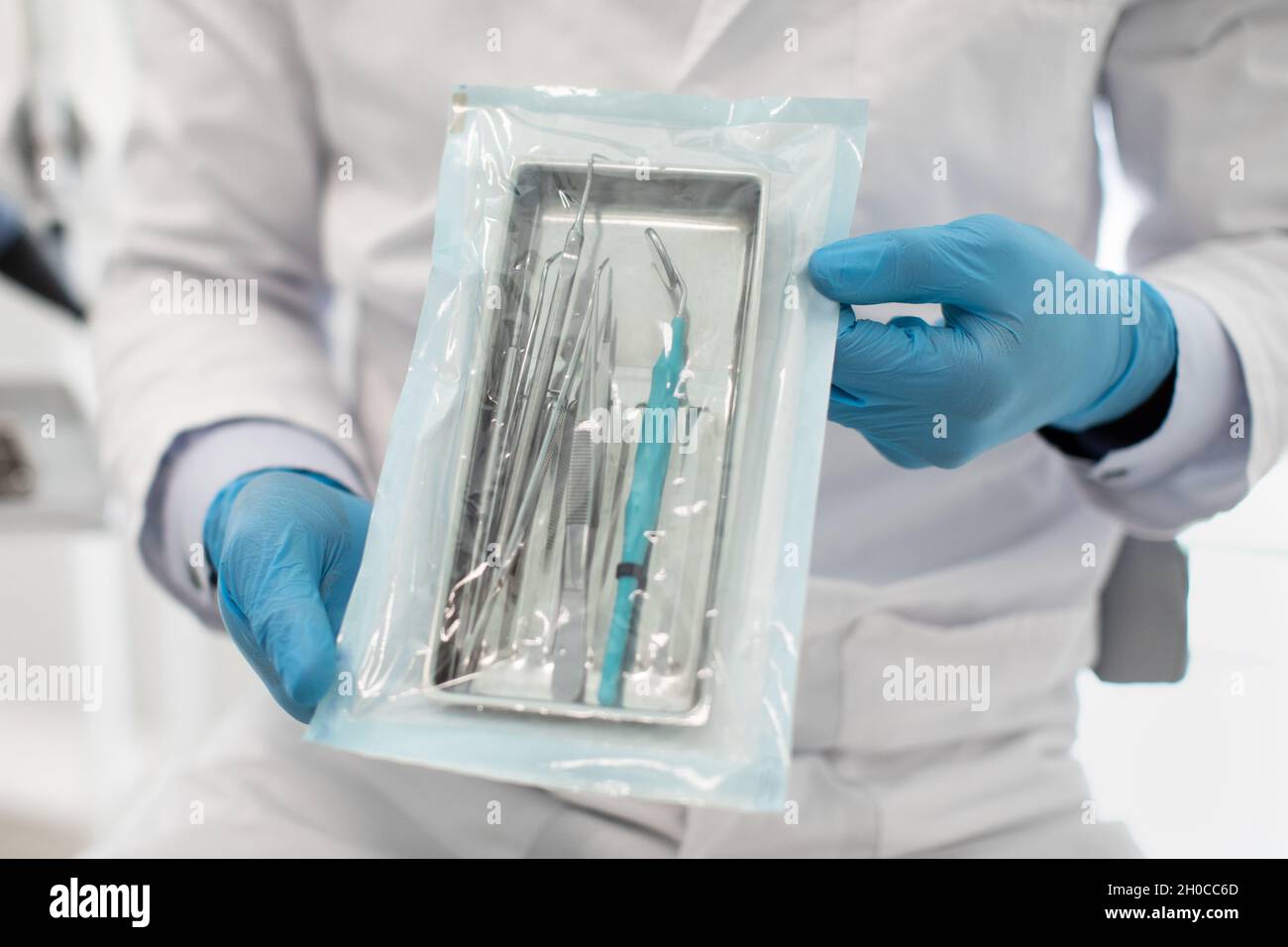 Doctor Wearing Blue Sterile Gloves Demonstating Sealed Sterilization Pouch With Dental Tools
