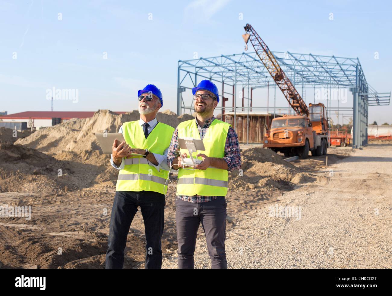 Two engineers with helmets and vests operating with drone by remote ...