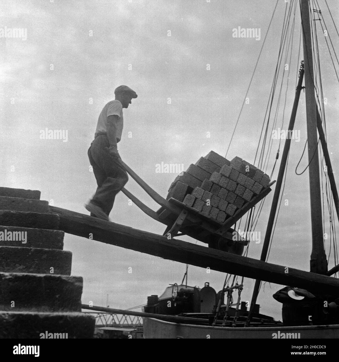 Ein Arbeiter am Rhein mit seiner Schubkarre, Deutschland 1930er Jahre. A worker at river Rhine with his barrow, Germany 1930s. Stock Photo