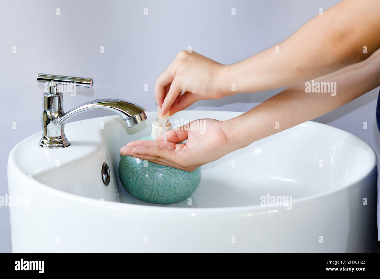 Hand pressing a bottle of hand soap pump on a clean white round sink