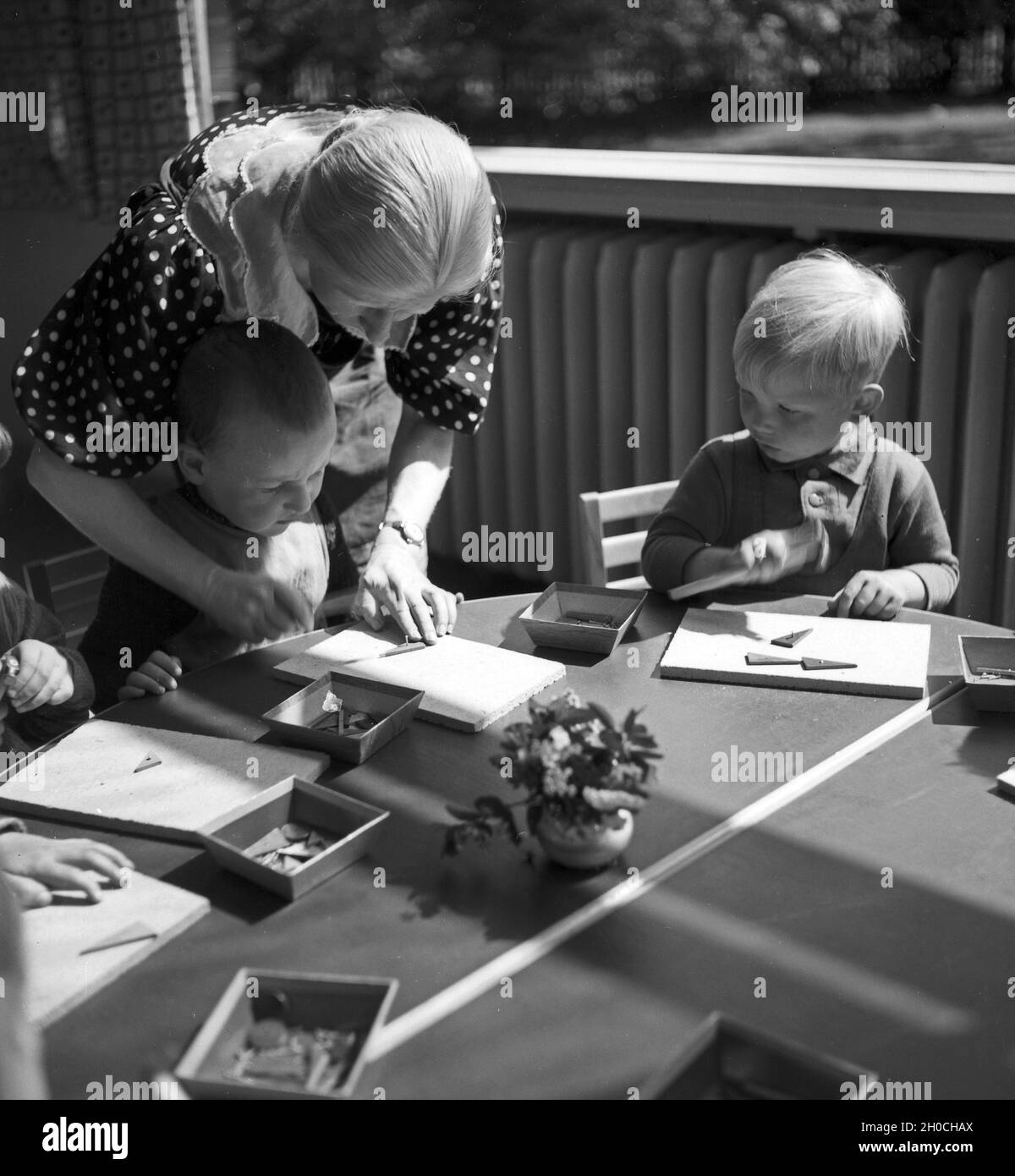 Eine Kindergärtnerin kümmert sich um die kleinen Kinder im Kindergarten, Deutschland 1930er Jahre. A nursery teacher with her children group at the Kindergarten, Germany 1930s. Stock Photo