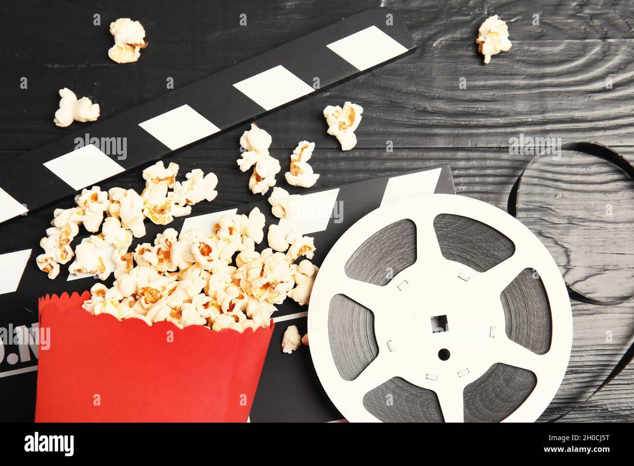 Tasty popcorn, film reel and clapperboard on wooden background, top