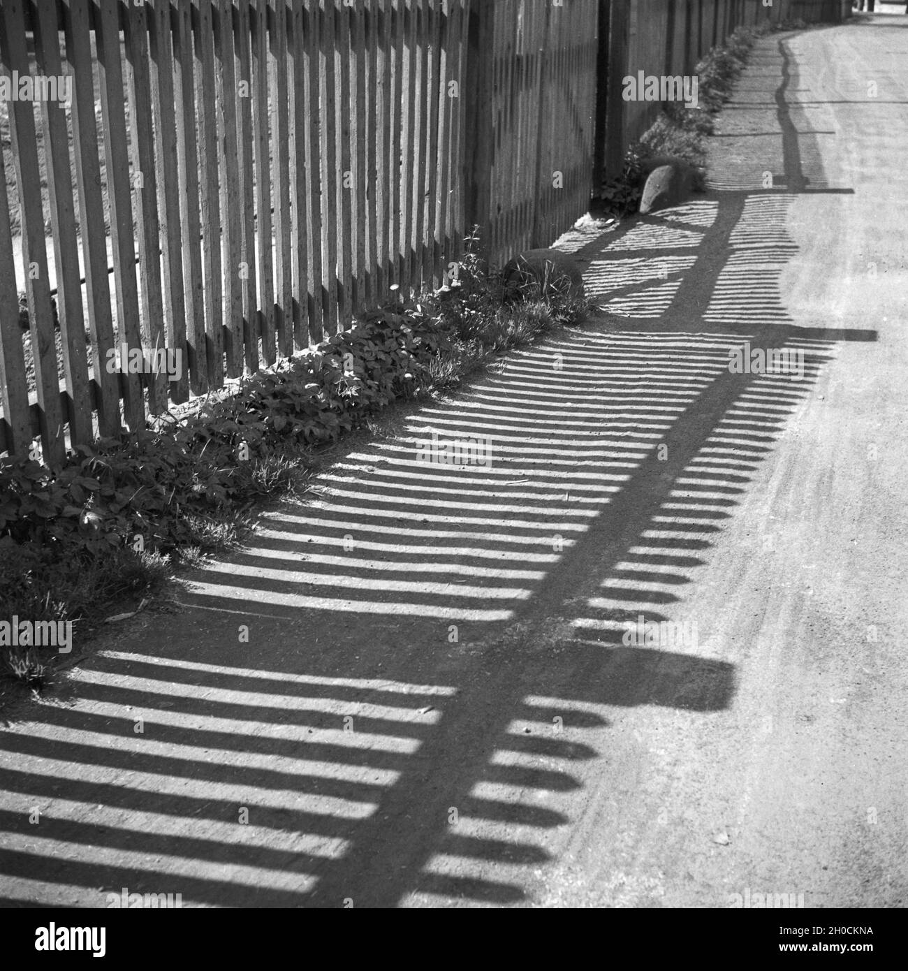 Licht und Schatten von einem Zaun auf einer Dorfstraße, Deutschland 1930er Jahre. Light and shadow from a fence on a village path, Germany 1930s. Stock Photo