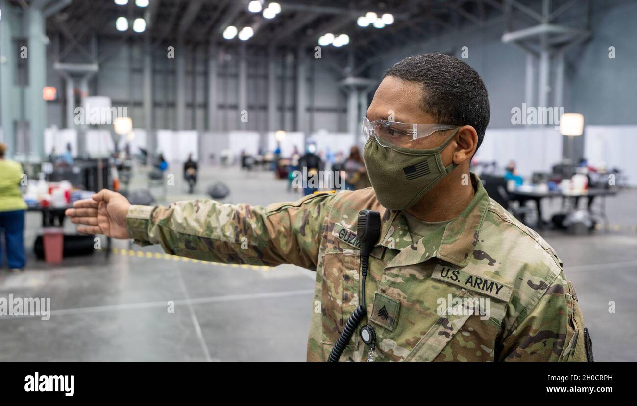 U.S. Army Sgt. Levinc Guzman, a wheeled vehicle mechanic assigned to the 719th Composite Truck Company, 369th Sustainment Brigade, 53rd Troop Command, directs NY residents from the vaccination lines after registration check-in to the his Soldiers who will direct them to a vaccination station, in support of state efforts to provide mass COVID-19 vaccinations administered by the New York State Department of Health at the Javits Convention Center in Manhattan, New York, January 26, 2021.    The National Guard has more than 350 Guardsmen and women deployed to the vaccination site to support staffi Stock Photo