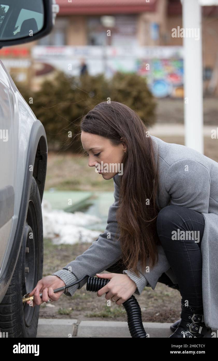 Pretty young woman driver filling air in tires of car on gas station