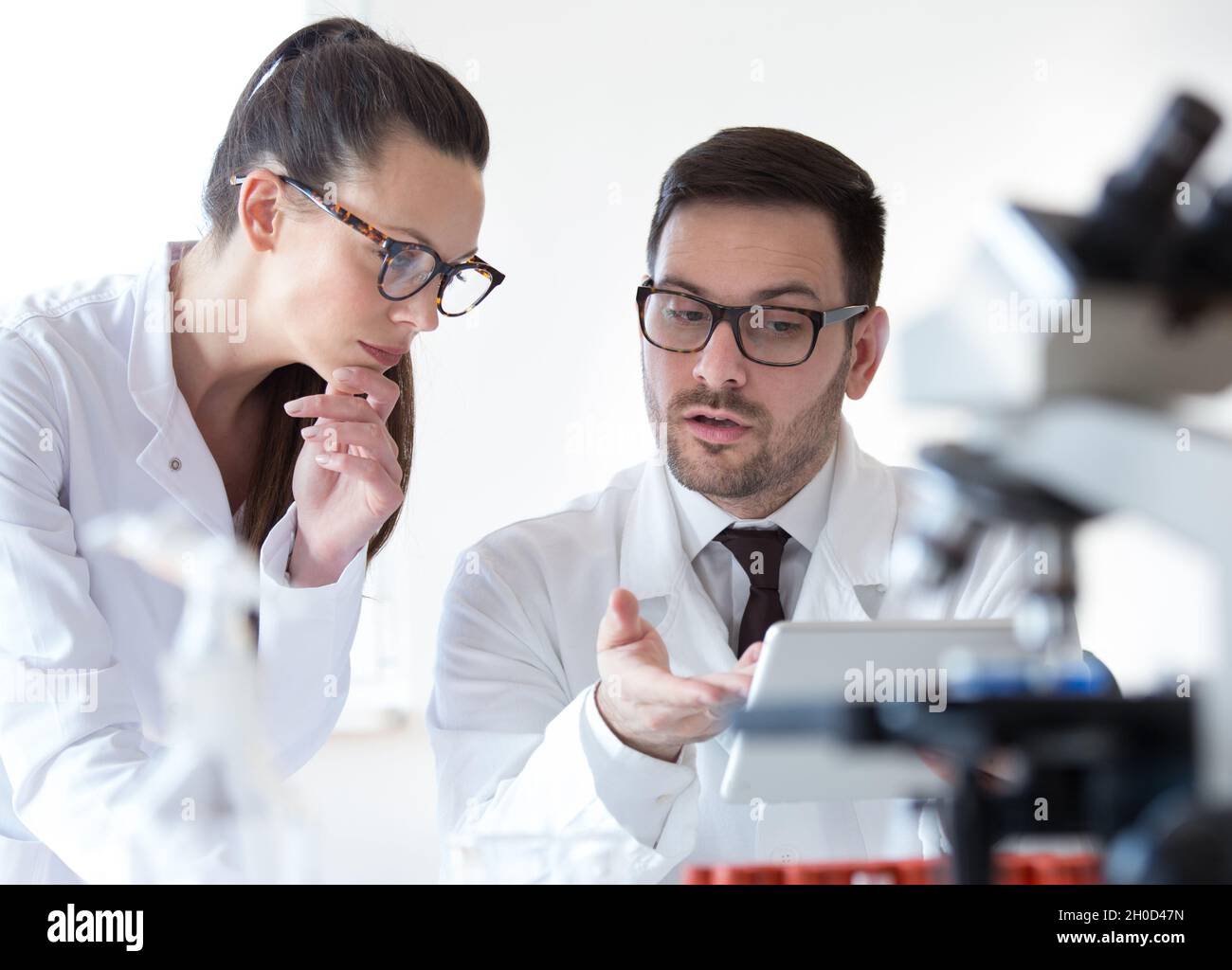 Man and woman scientists looking at tablet and analyzing data from microscope test Stock Photo