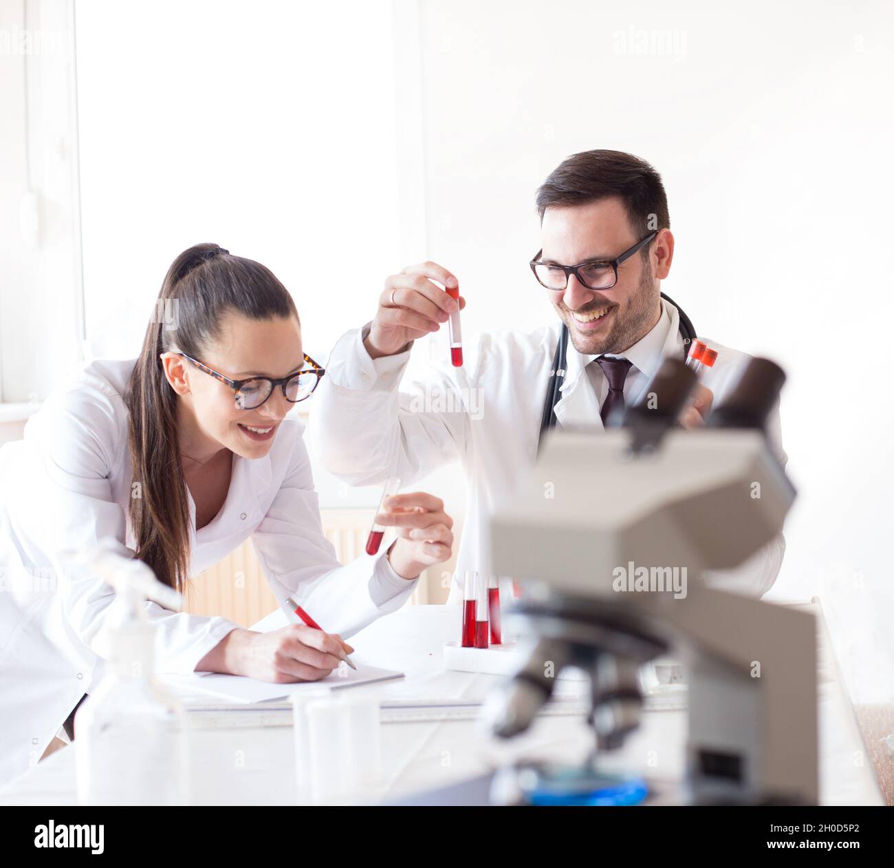 Man and woman scientists looking at tablet and analyzing data from microscope test Stock Photo