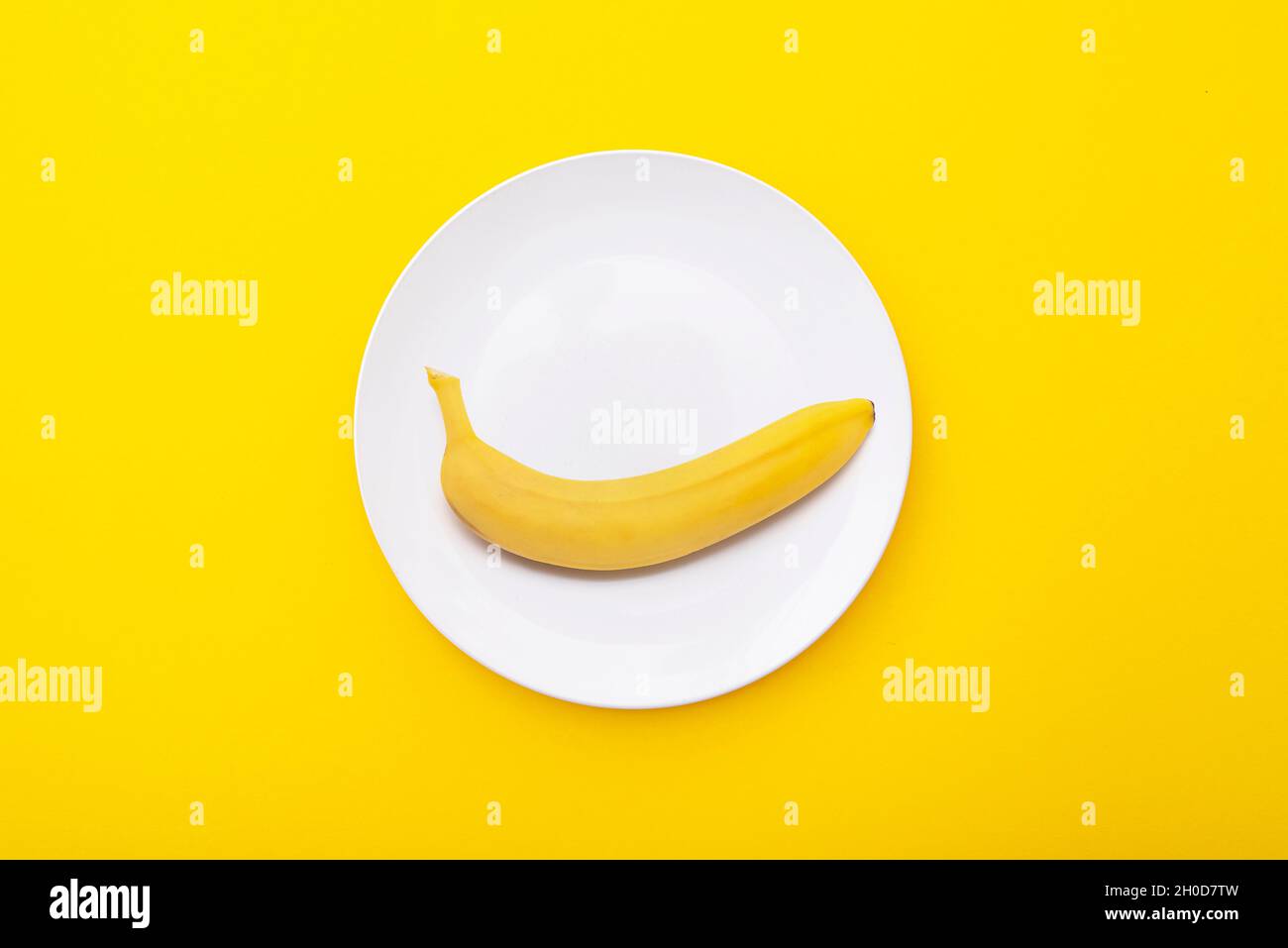 Bright yellow banana on white ceramic plate. Creative minimal composition with riple banana, top view Stock Photo