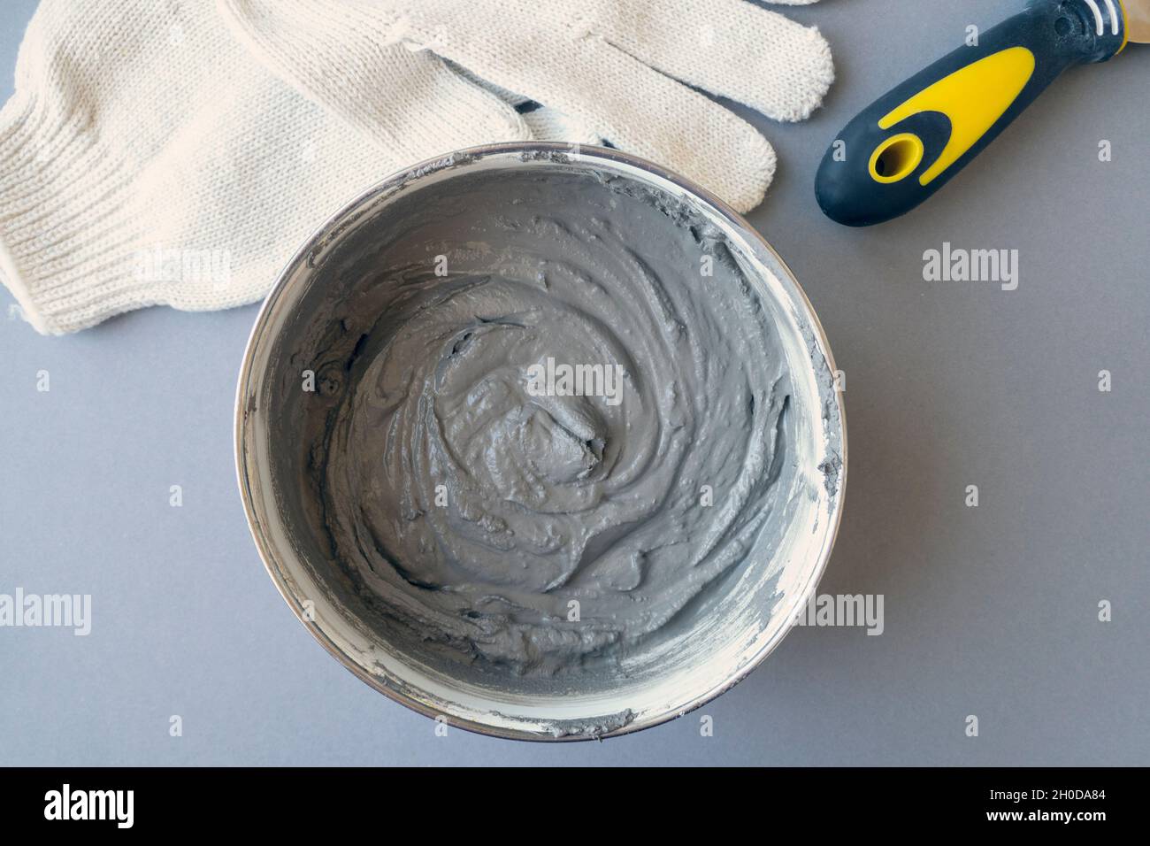 Worker equipment: container with cement, putty knife and workers gloves on a desk, top view Stock Photo