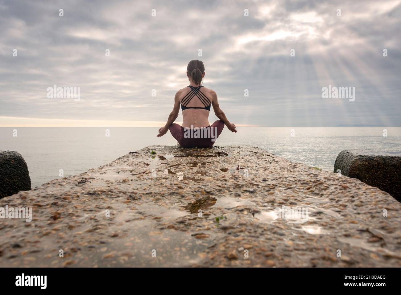Rear view of a woman sitting meditating by the sea, practicing yoga ...