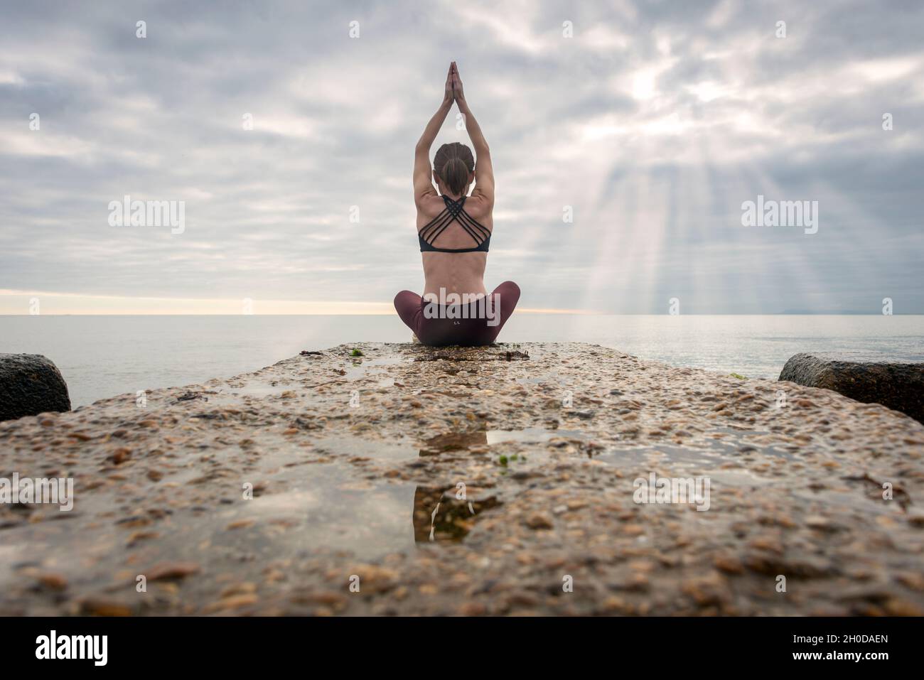 Rear view of a woman sitting meditating by the sea, practicing yoga ...