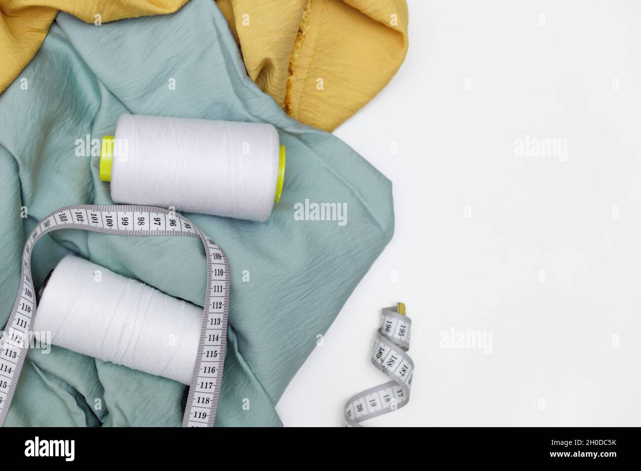 Various fabrics, measuring tape and thread isolated on white. Flat lay Stock Photo