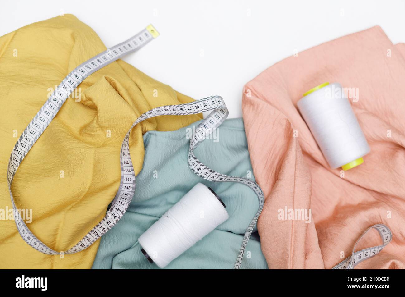 Various fabrics, measuring tape and thread isolated on white. Flat lay Stock Photo