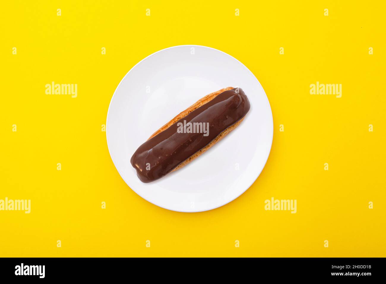 Chocolate eclair on the ceramic plate with bright yellow surface. Minimal composition. Top view. Stock Photo