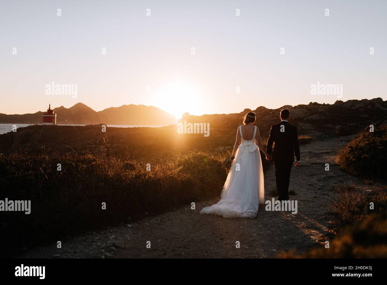 Just married couple walking towards a lighthouse at sunset Stock Photo ...