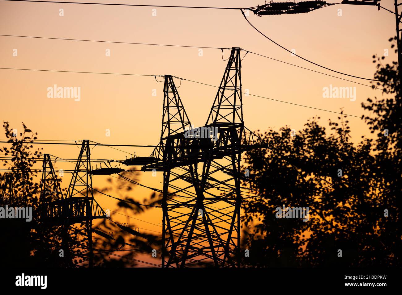 Silhouettes of high voltage pylons against the orange sky during sunset. Photo taken at dusk under natural lighting conditions Stock Photo