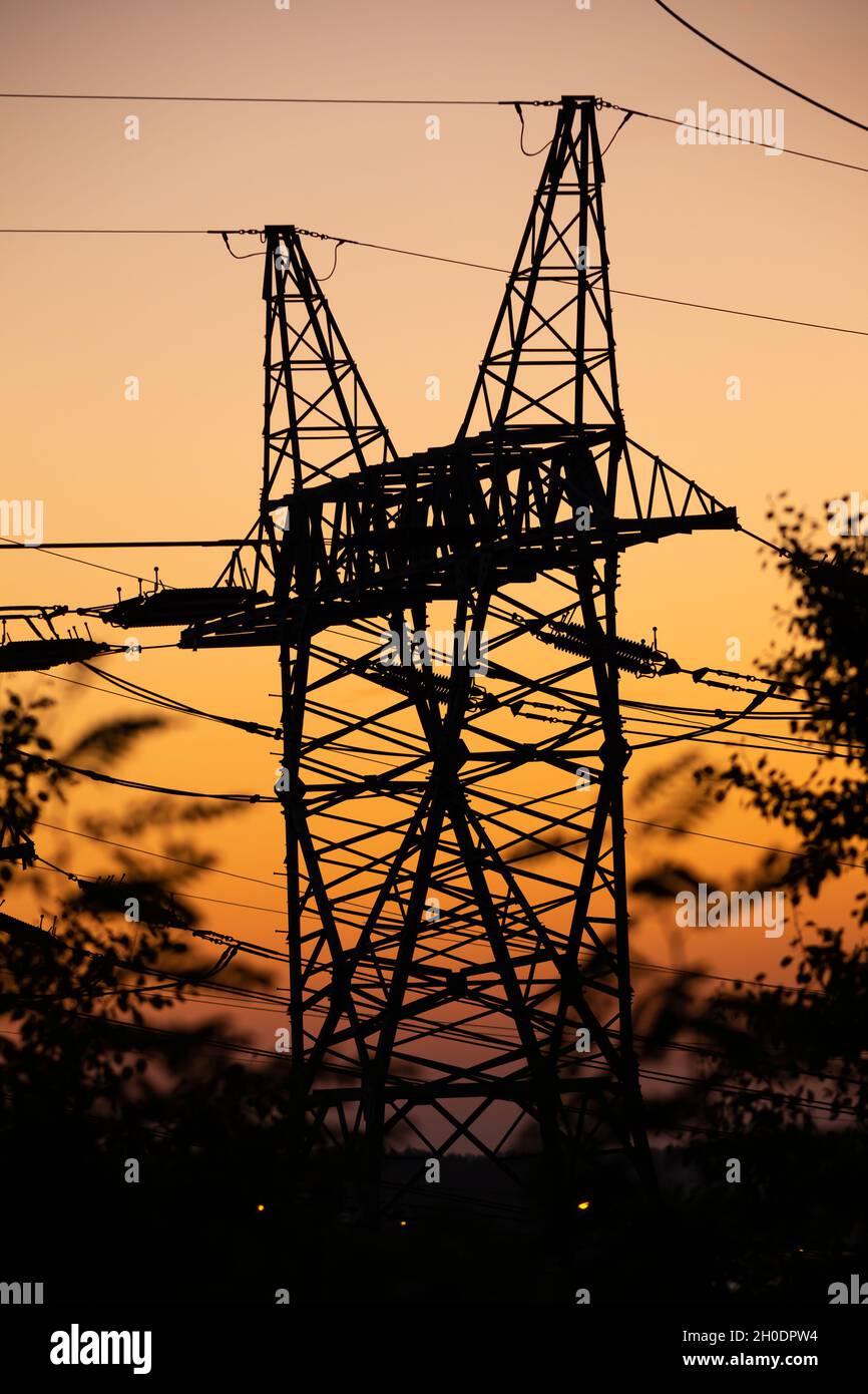 Silhouettes of high voltage pylons against the orange sky during sunset. Photo taken at dusk under natural lighting conditions Stock Photo