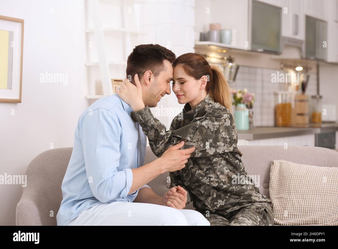Woman in military uniform with her husband on sofa at home Stock Photo