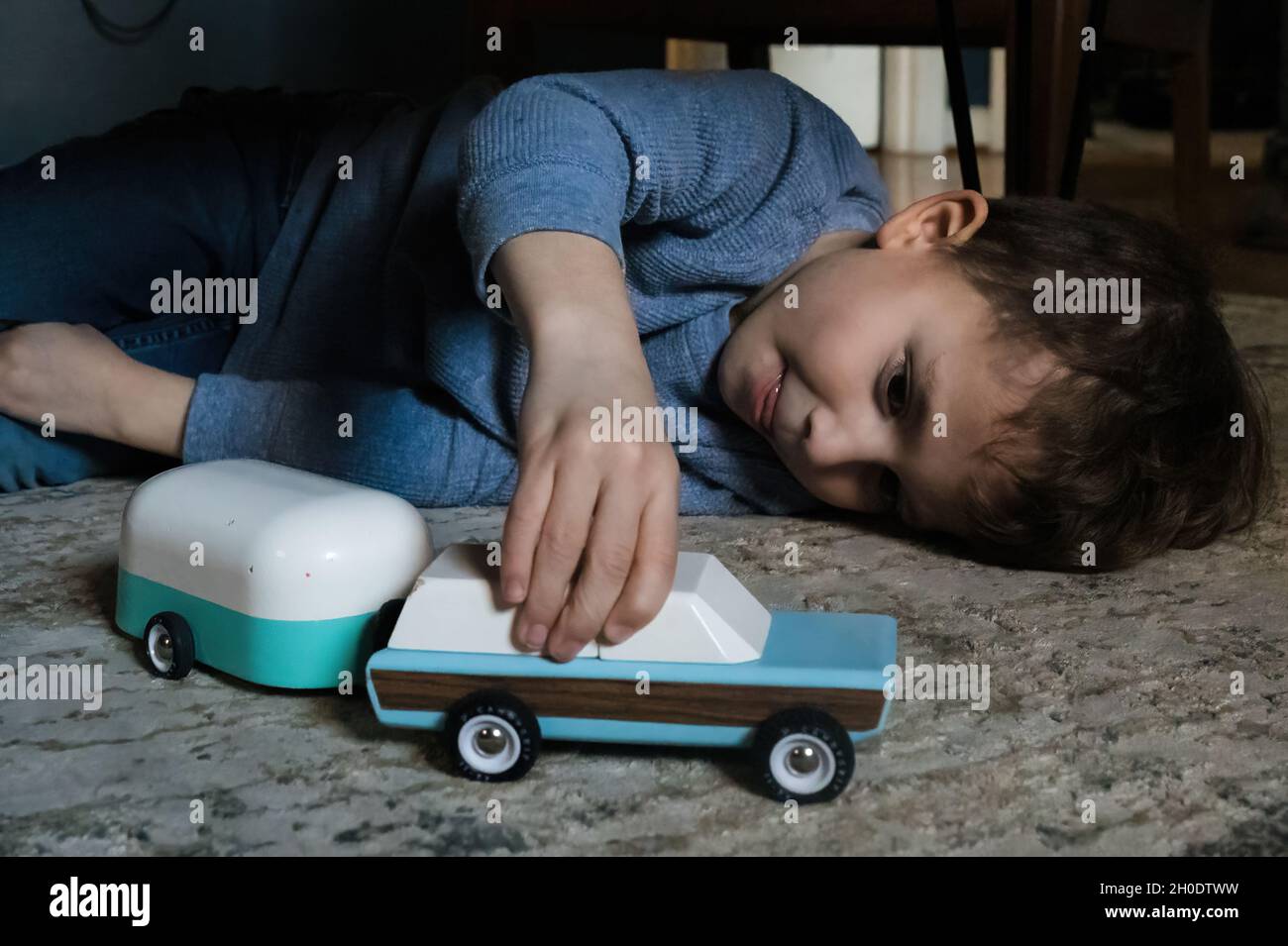 Boy playing with toy car and camper on the living room rug Stock Photo