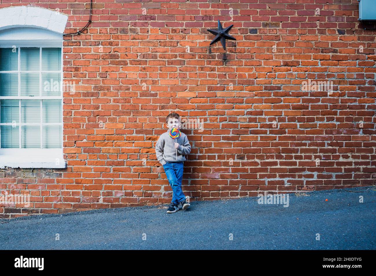 Little boy with lollipop leaning against a brick wall Stock Photo