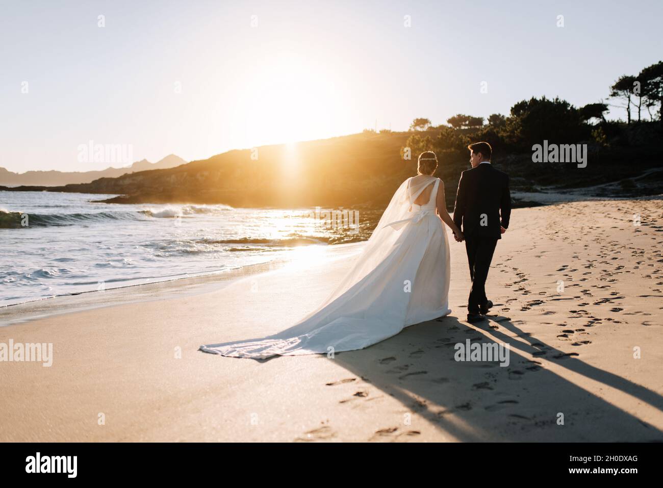 Just married couple walking by the beach at sunset Stock Photo - Alamy