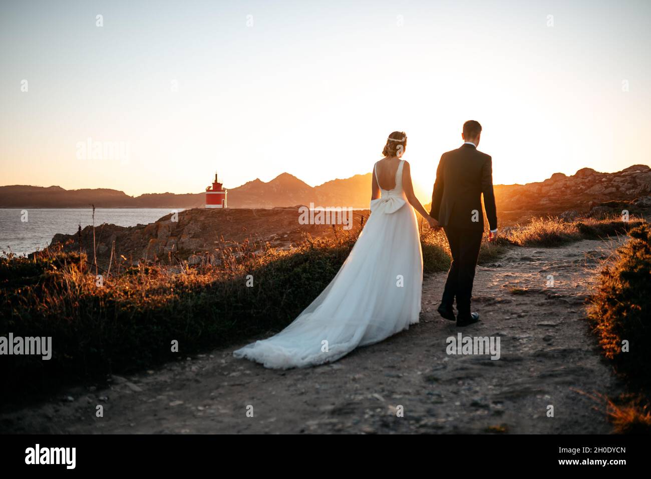 Just married couple walking towards a lighthouse at sunset Stock Photo ...