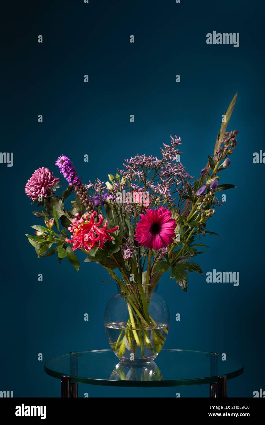 Fresh bouquet of flowers in a glass vase on a glass table with a dark blue background Stock Photo